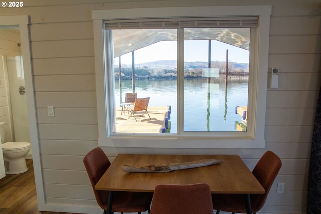 dining area featuring a water view, wood walls, and wood finished floors