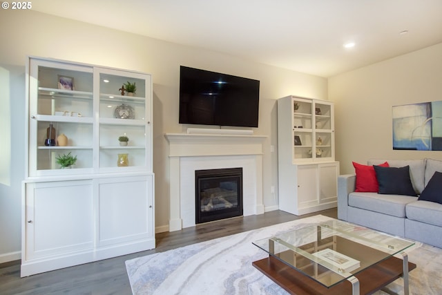 living area with recessed lighting, a glass covered fireplace, and wood finished floors