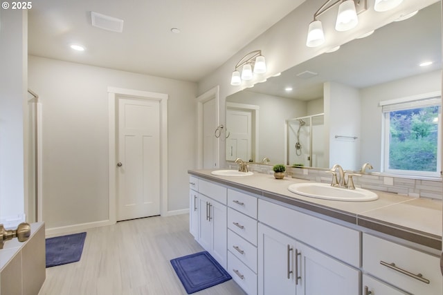 full bath featuring baseboards, a sink, double vanity, and a shower stall