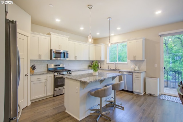 kitchen with backsplash, appliances with stainless steel finishes, wood finished floors, a sink, and white cabinets