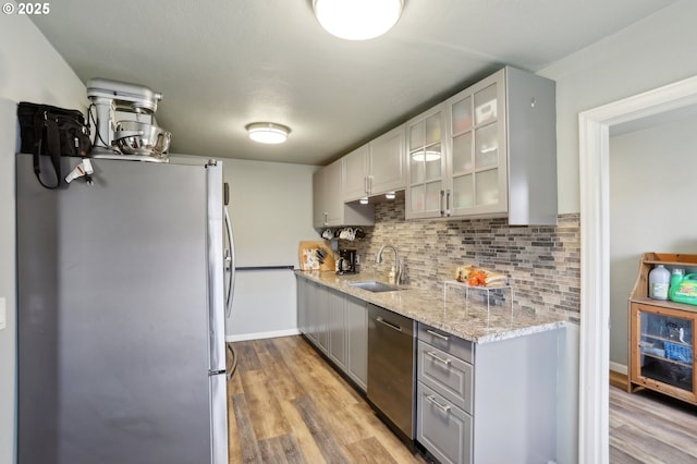 kitchen with appliances with stainless steel finishes, sink, light hardwood / wood-style flooring, and decorative backsplash