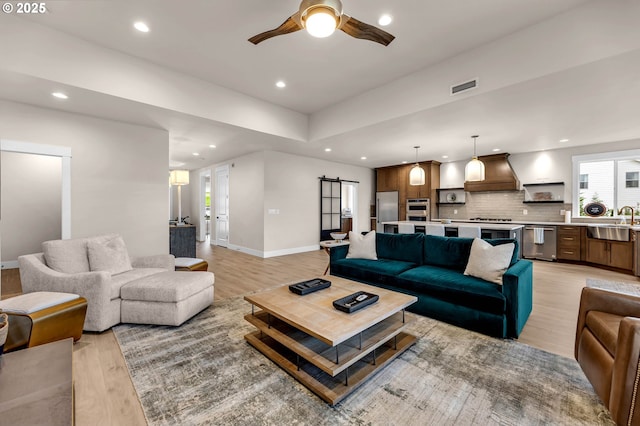 living area featuring recessed lighting, a ceiling fan, a barn door, light wood-style floors, and visible vents