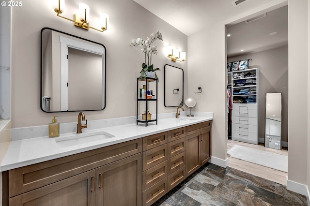 full bathroom with a sink, a walk in closet, baseboards, and double vanity