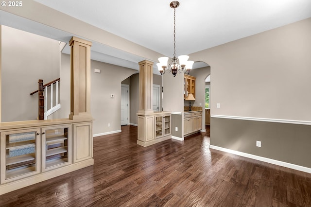 unfurnished dining area featuring decorative columns, a chandelier, and dark hardwood / wood-style floors