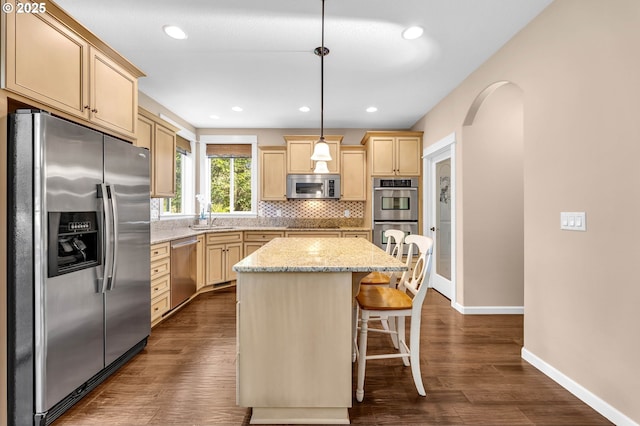 kitchen with appliances with stainless steel finishes, decorative backsplash, sink, a kitchen island, and pendant lighting