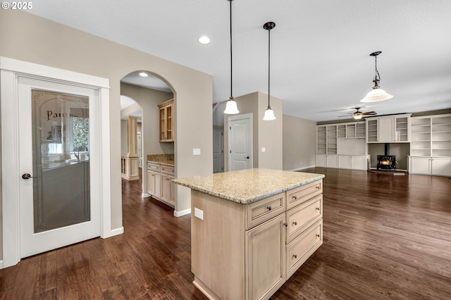 kitchen with a center island, light stone countertops, built in shelves, pendant lighting, and dark wood-type flooring