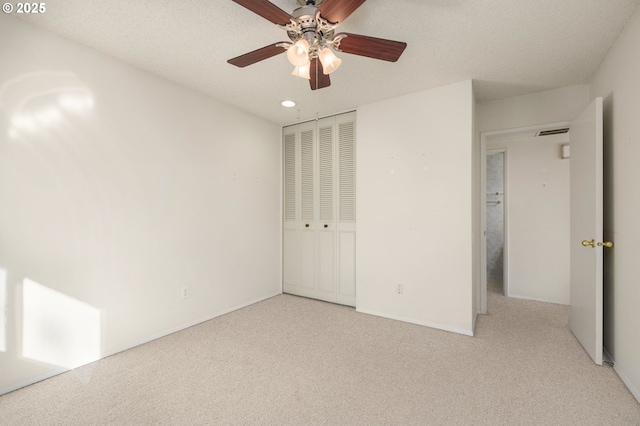 unfurnished bedroom featuring ceiling fan, light colored carpet, a closet, and a textured ceiling