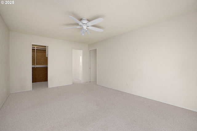 unfurnished bedroom featuring a walk in closet, a closet, ceiling fan, and carpet