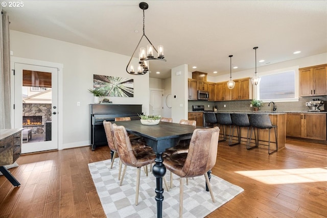 dining space with sink, a notable chandelier, a fireplace, and light wood-type flooring