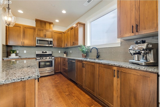 kitchen with decorative light fixtures, sink, dark hardwood / wood-style flooring, stainless steel appliances, and light stone countertops