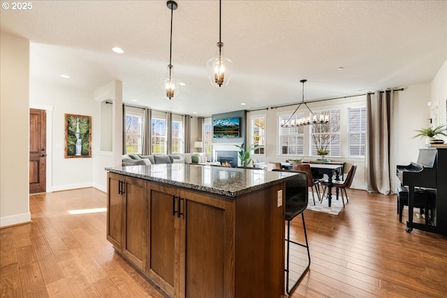 kitchen with dark stone countertops, hanging light fixtures, light hardwood / wood-style floors, and a center island