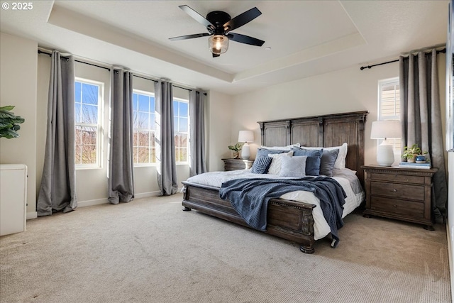 bedroom featuring a raised ceiling, light carpet, and ceiling fan