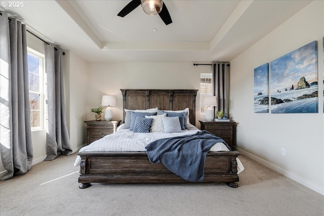 bedroom with light carpet, ceiling fan, and a tray ceiling