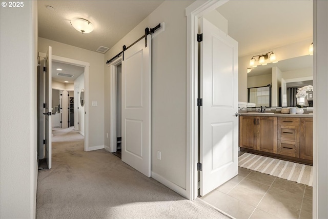 hall featuring sink, light colored carpet, and a barn door