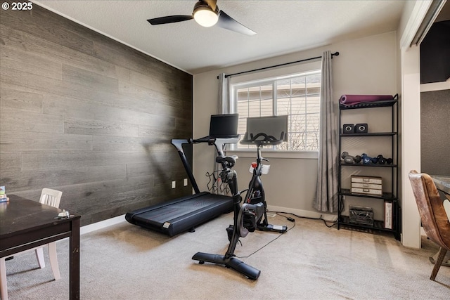 exercise room featuring ceiling fan, light colored carpet, and wooden walls