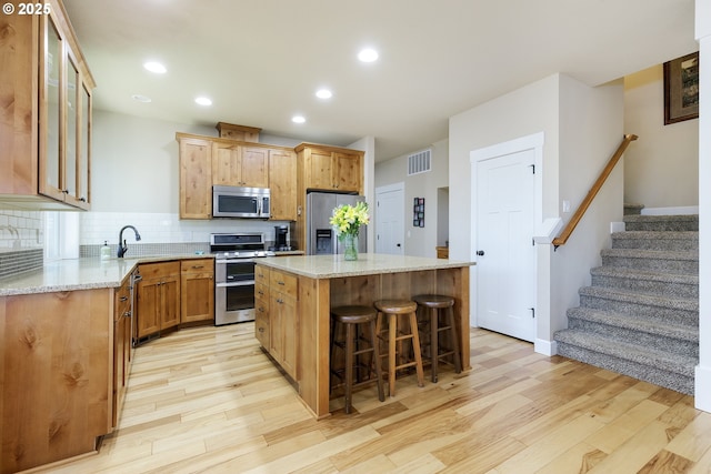 11862 White Ln, Oregon City, OR 97045 - kitchen with appliances with stainless steel finishes, light wood-style flooring, a kitchen island, tasteful backsplash, and a kitchen breakfast bar
