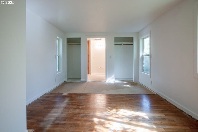 unfurnished bedroom with two closets, wood finished floors, and baseboards