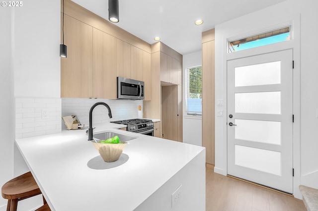 kitchen with a sink, backsplash, appliances with stainless steel finishes, a peninsula, and light countertops