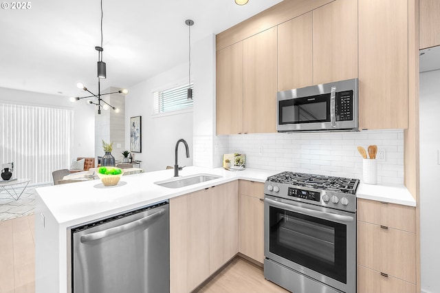 kitchen with a sink, a peninsula, light brown cabinetry, and stainless steel appliances