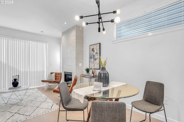 dining area with light wood-style flooring, recessed lighting, a fireplace, baseboards, and a chandelier