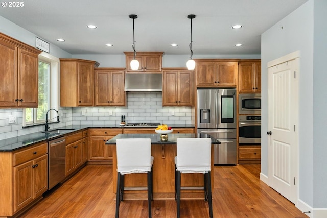 kitchen with under cabinet range hood, appliances with stainless steel finishes, wood finished floors, and a sink