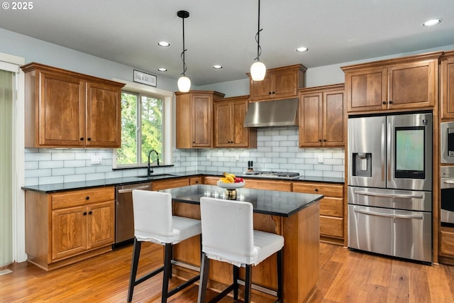 kitchen with under cabinet range hood, light wood-style floors, appliances with stainless steel finishes, and a sink