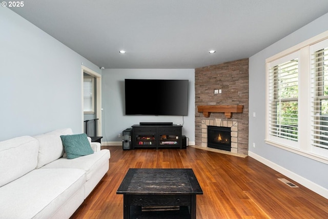 living area with visible vents, a stone fireplace, baseboards, and wood finished floors