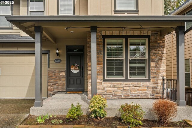 view of exterior entry with a garage, stone siding, and a porch