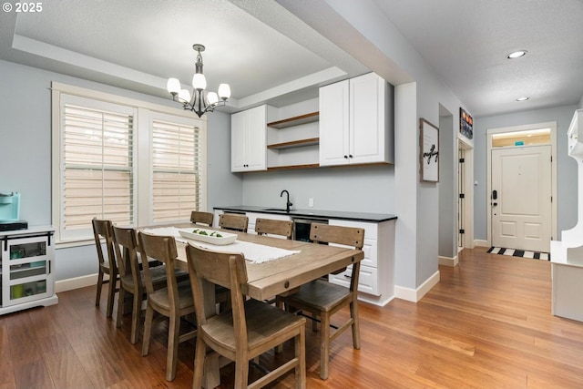 dining space with a tray ceiling, baseboards, an inviting chandelier, and light wood finished floors