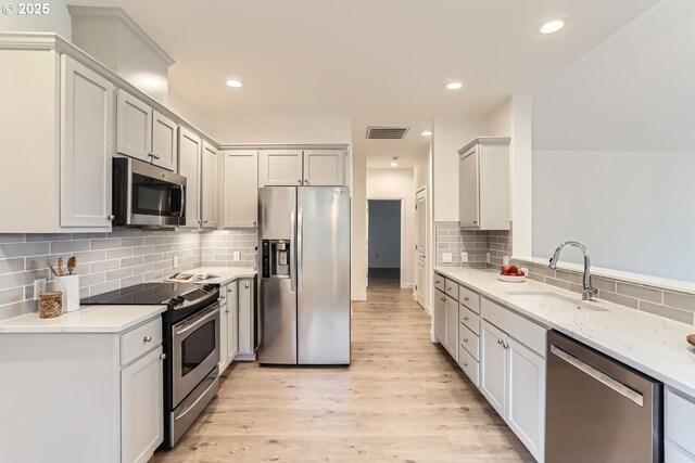 kitchen featuring visible vents, decorative backsplash, light wood-style flooring, stainless steel appliances, and a sink