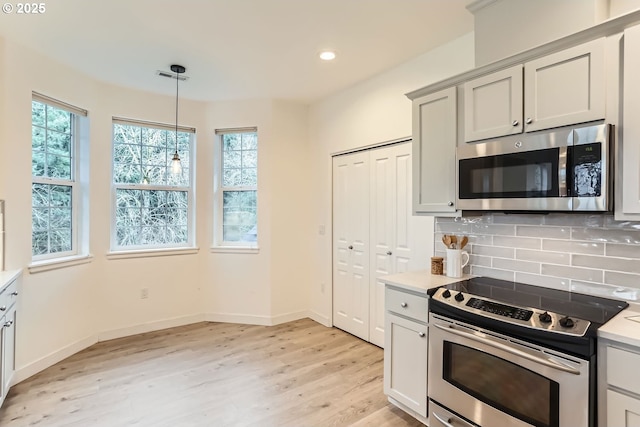 kitchen featuring pendant lighting, stainless steel appliances, tasteful backsplash, light countertops, and light wood-style floors