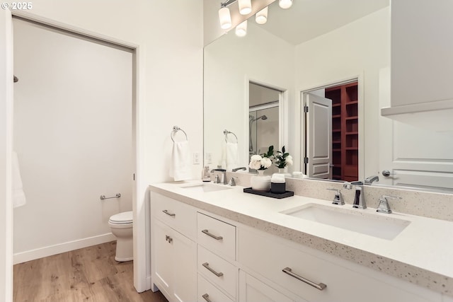 full bath with toilet, double vanity, a sink, and wood finished floors