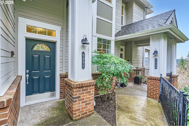 entrance to property featuring a porch, roof with shingles, and brick siding