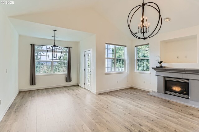 unfurnished living room with a chandelier, high vaulted ceiling, a tile fireplace, wood finished floors, and baseboards