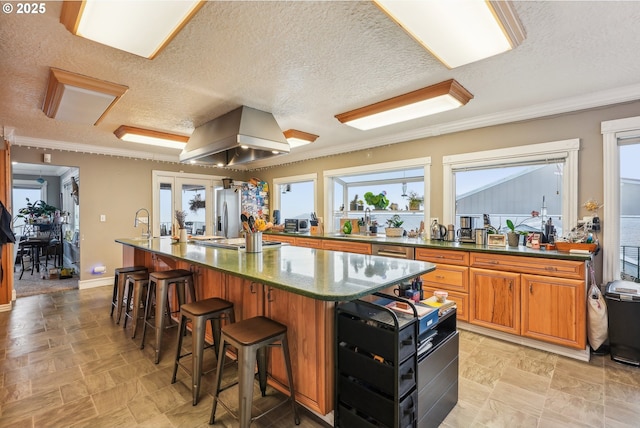 kitchen featuring a breakfast bar, island range hood, sink, stainless steel fridge, and a spacious island