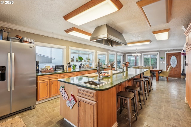 kitchen with a breakfast bar, pendant lighting, island exhaust hood, stainless steel refrigerator with ice dispenser, and a center island with sink