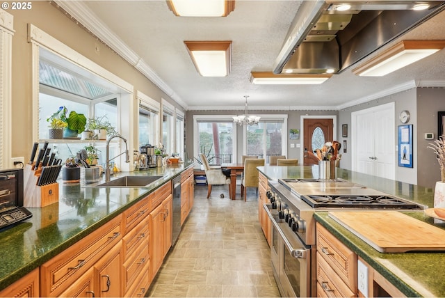 kitchen with pendant lighting, sink, crown molding, wall chimney range hood, and stainless steel appliances