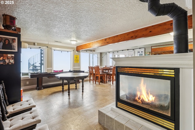 game room featuring beamed ceiling, a textured ceiling, and a multi sided fireplace