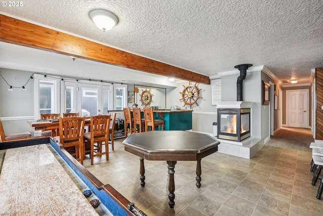 game room featuring beamed ceiling, ornamental molding, a wood stove, and a textured ceiling