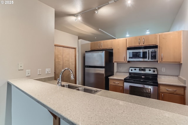 kitchen with light stone counters, a peninsula, stainless steel appliances, light brown cabinets, and a sink