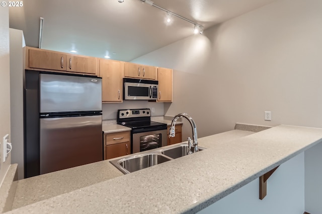 kitchen with appliances with stainless steel finishes, a peninsula, light stone countertops, light brown cabinetry, and a sink