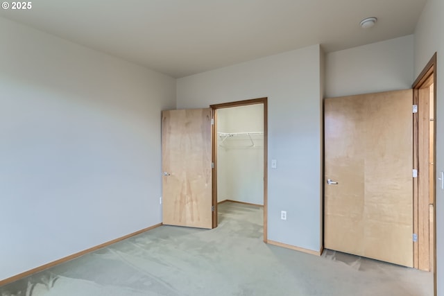 unfurnished bedroom with light carpet, a closet, a walk in closet, and baseboards