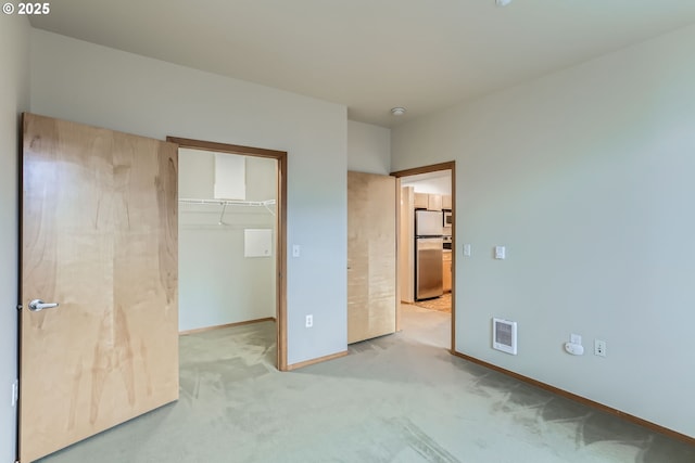 unfurnished bedroom with a walk in closet, visible vents, light carpet, stainless steel fridge, and baseboards