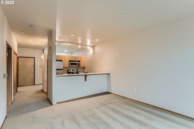 kitchen featuring light carpet, appliances with stainless steel finishes, a peninsula, light countertops, and light brown cabinetry