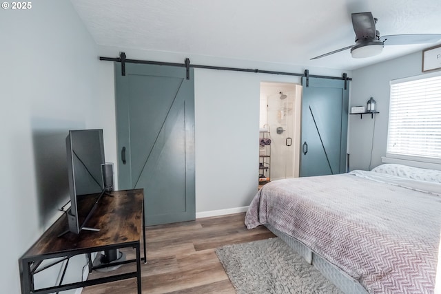 bedroom with a ceiling fan, a barn door, baseboards, and wood finished floors