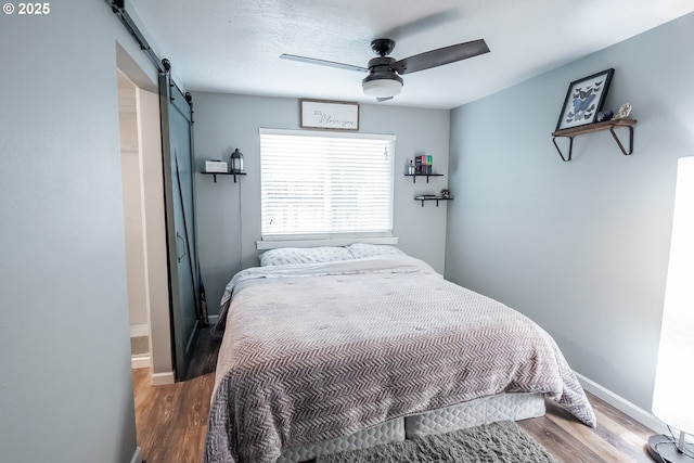 bedroom featuring a ceiling fan, wood finished floors, baseboards, and a barn door