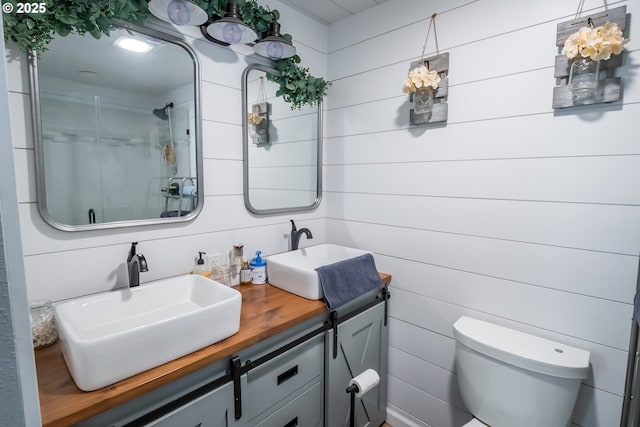 bathroom with toilet, double vanity, an enclosed shower, and a sink