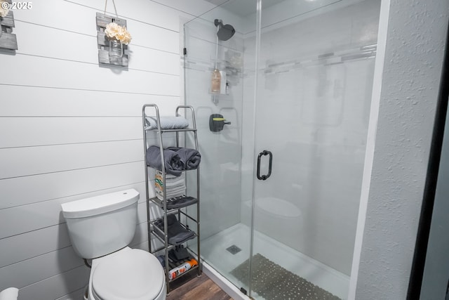 bathroom with toilet, a stall shower, and wood finished floors