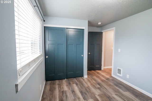 unfurnished bedroom featuring visible vents, a closet, baseboards, and wood finished floors