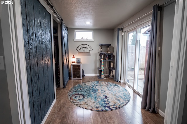 interior space with a textured ceiling, a barn door, wood finished floors, and baseboards